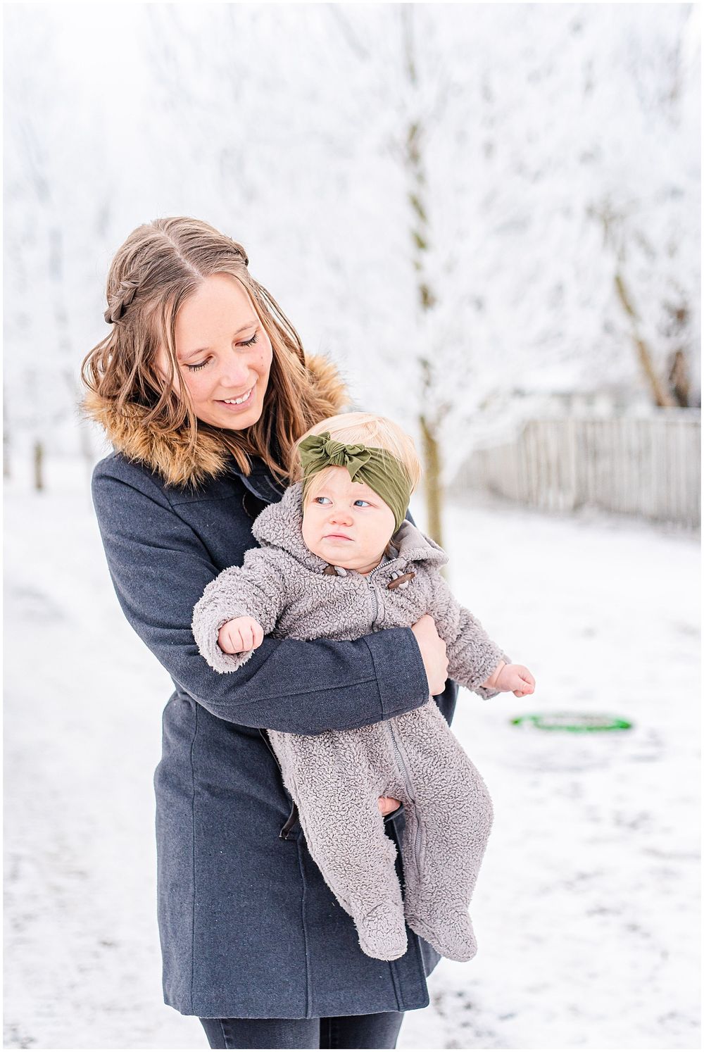 Woman in navy coat holding baby in warm winter outfit against snowy background.
