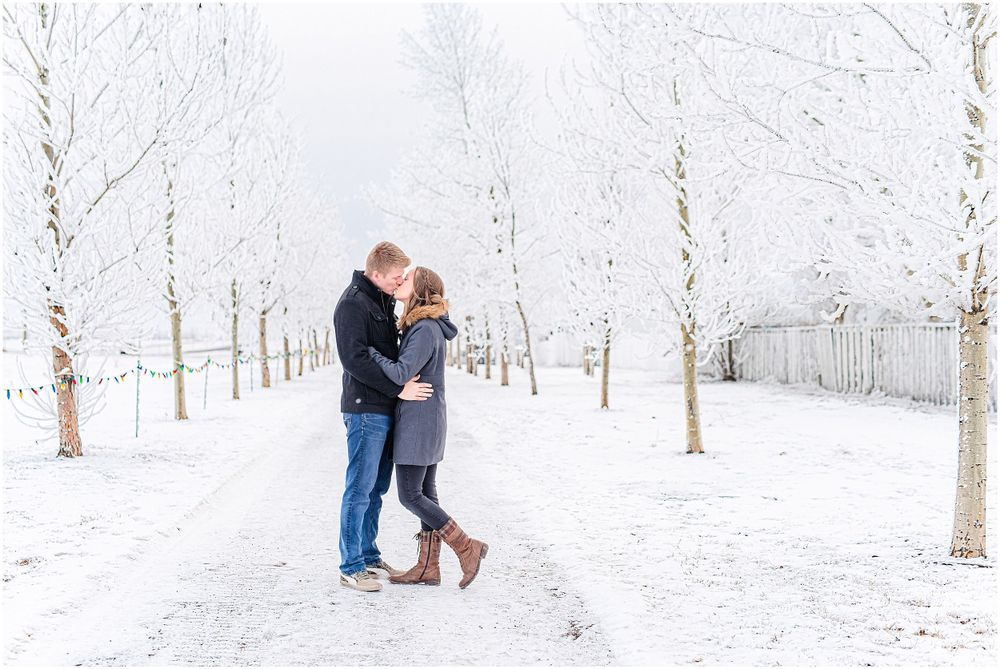 Couple embracing on snowy path surrounded by winter trees.