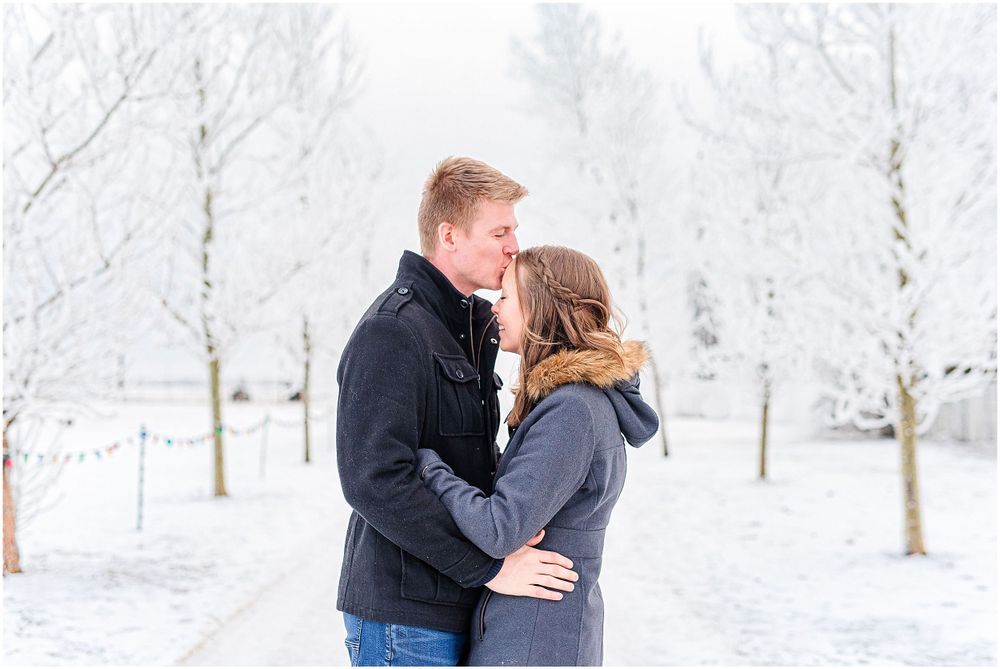 Intimate moment between couple in winter setting with snow-covered trees.