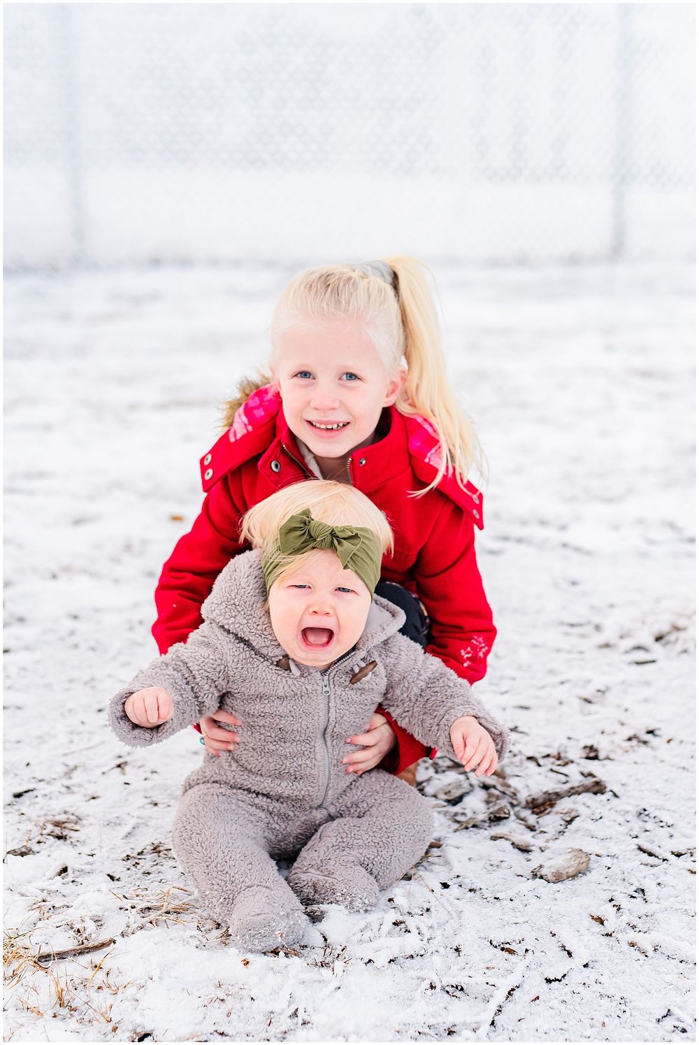 Two children playing in the snow with one wearing red coat and other in grey snowsuit.
