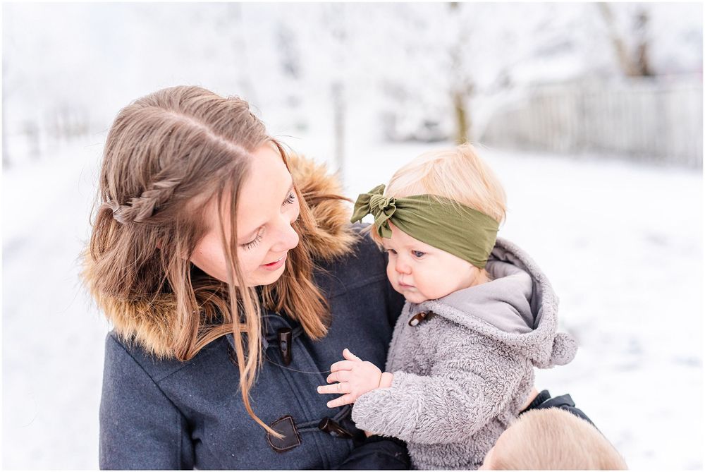 A tender winter moment between parent and child wearing warm coats in a snowy setting.