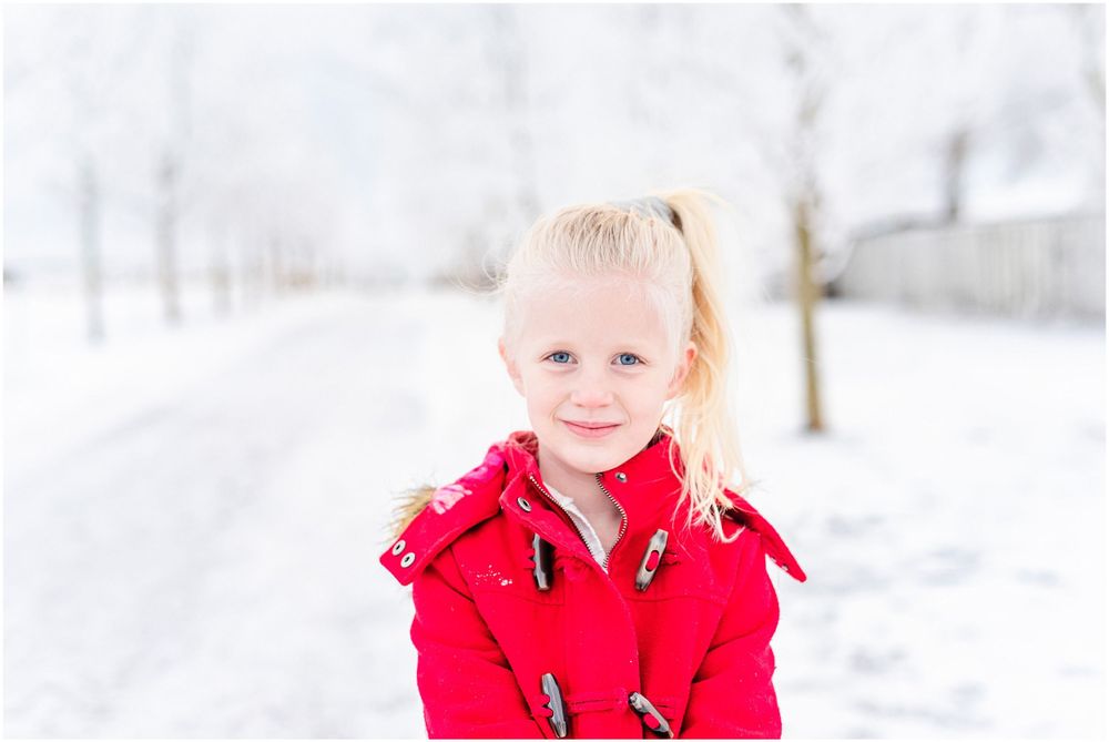 Child in bright red winter coat smiling against snowy winter background.