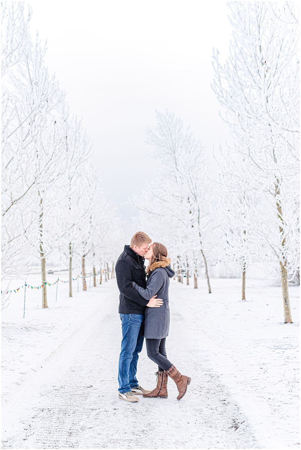 Couple embracing on a snowy path surrounded by frost-covered trees in winter.