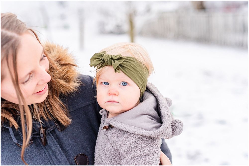Intimate winter moment between parent and baby wearing a green headband in the snow.