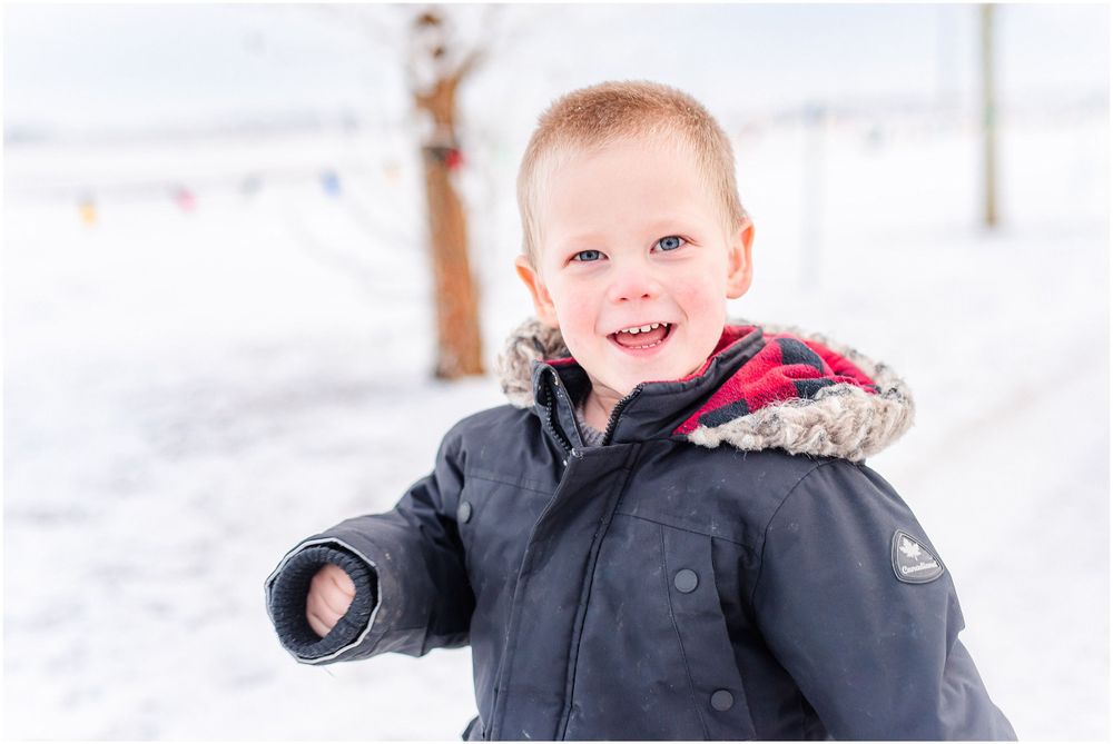 Happy child in winter coat smiling brightly against snowy background.