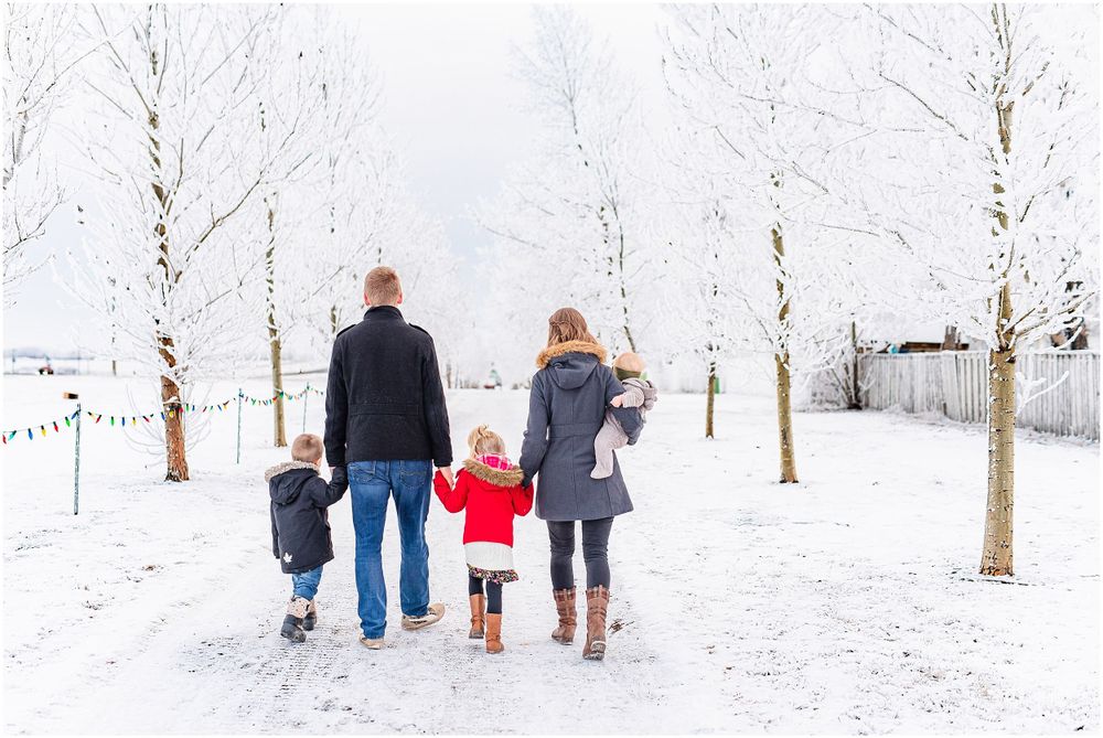 Family walking together on snowy path between white winter trees.