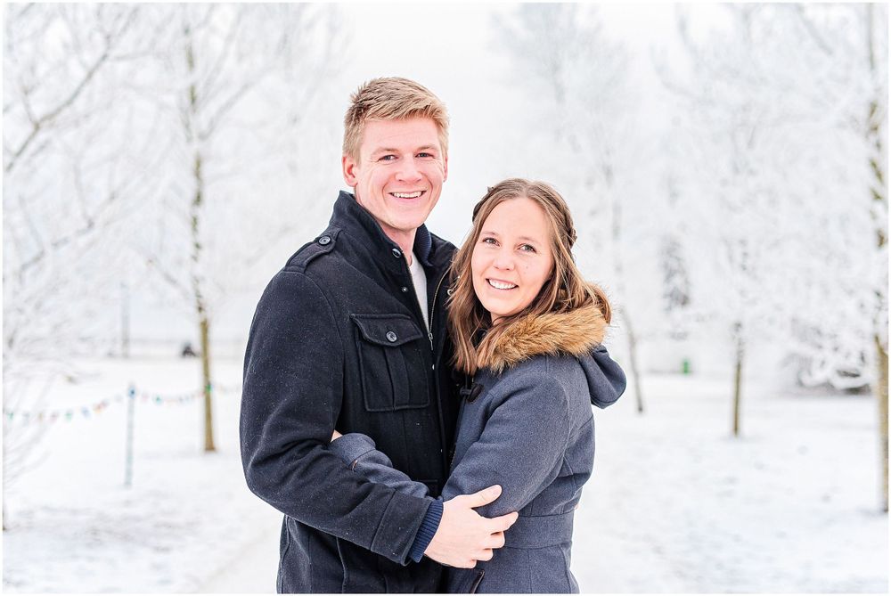 Couple in winter coats sharing embrace against snowy white winter backdrop.