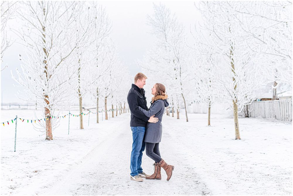 Romantic couple standing on snow-covered path between white winter trees.