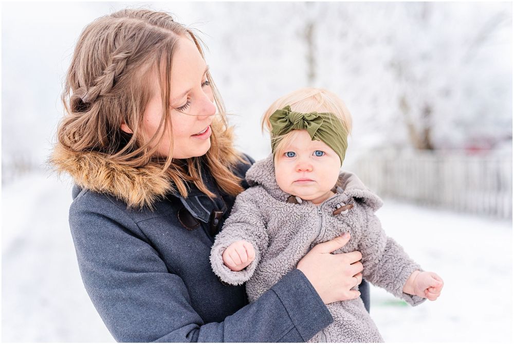 Parent holding baby in grey coat against snowy winter background.