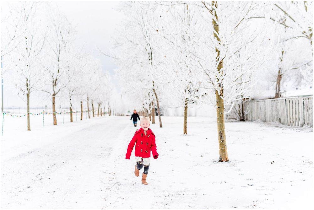 Child in red coat running down snowy path lined with frost-covered trees.