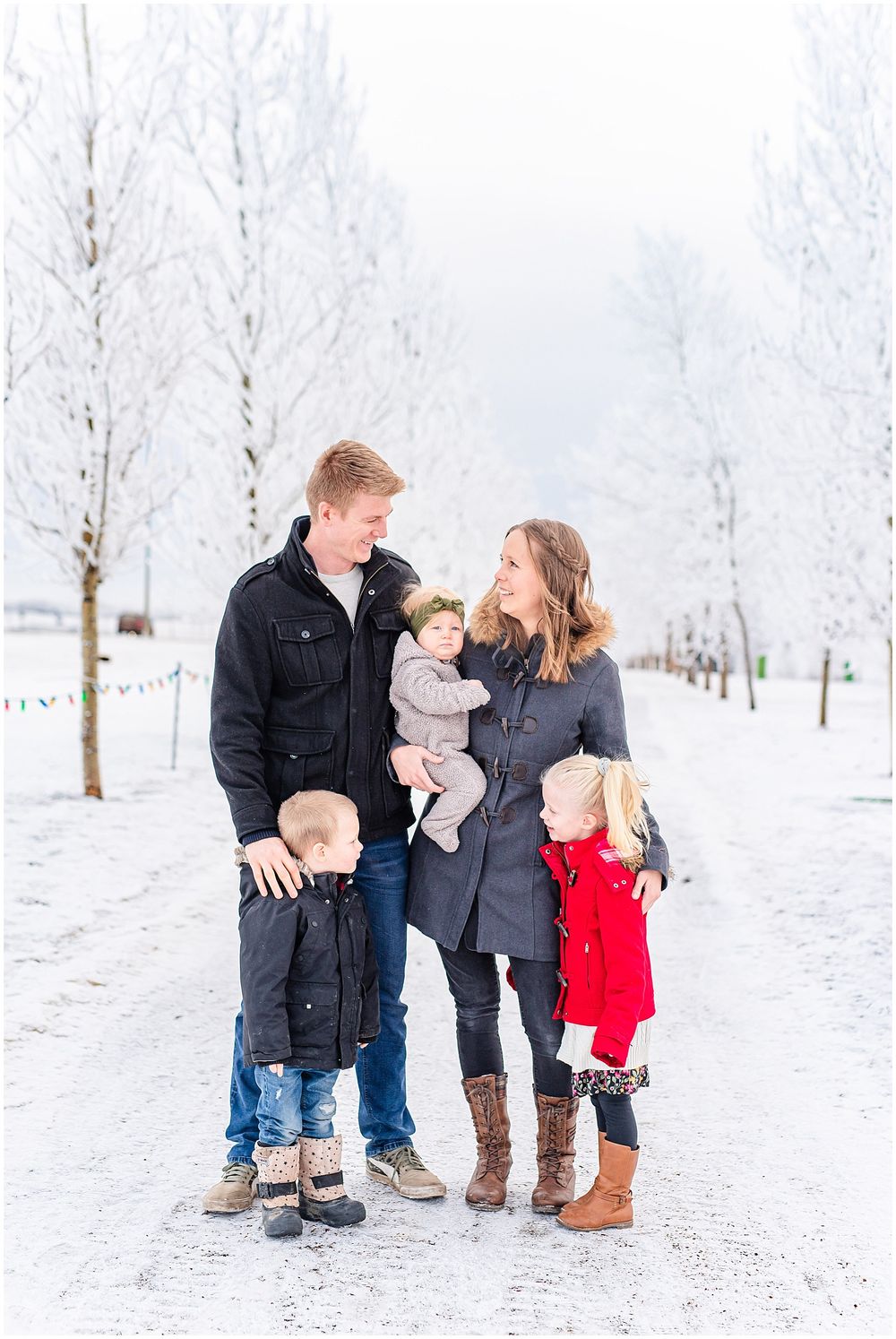 Family portrait on a snow-covered path surrounded by white winter trees.