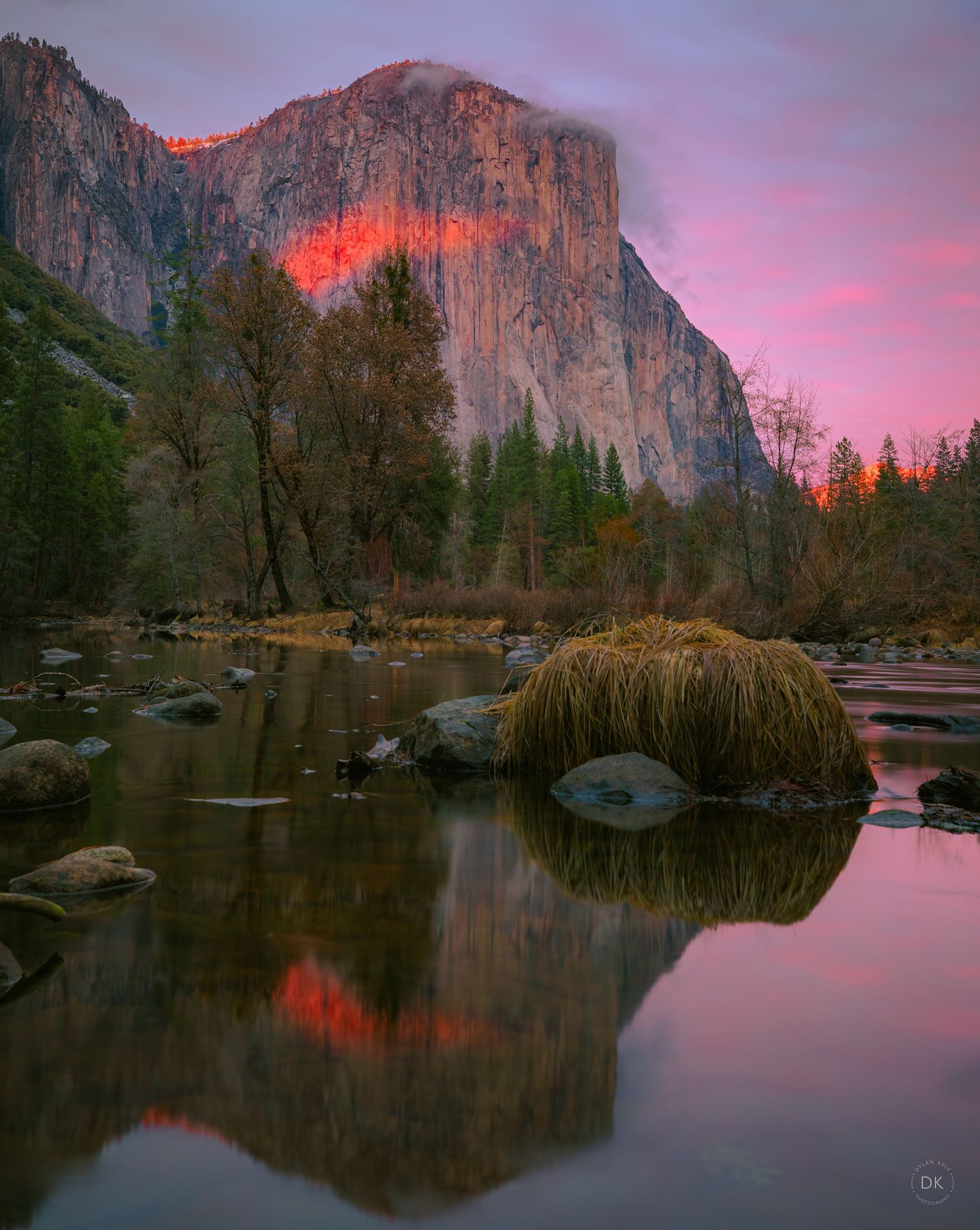 Dramatic sunset illuminates El Capitan in Yosemite National Park with pink skies reflecting in the calm Merced River waters.