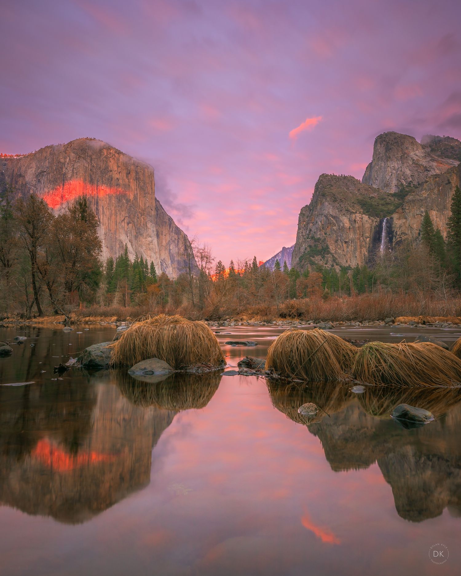 Stunning sunset reflection in Yosemite Valley with El Capitan and Bridalveil Fall towering over calm waters in winter.