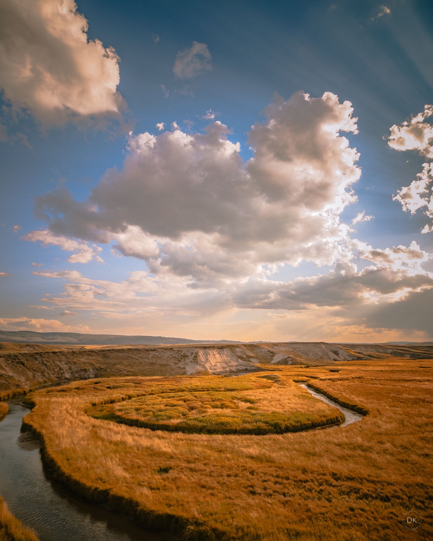 A winding river carves through golden grassland under dramatic sunset clouds in a scenic landscape view.