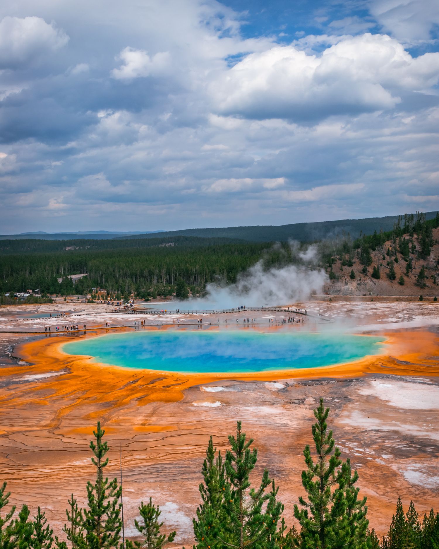 Vibrant Grand Prismatic Spring with turquoise water and orange bacterial mats in Yellowstone National Park under cloudy skies.