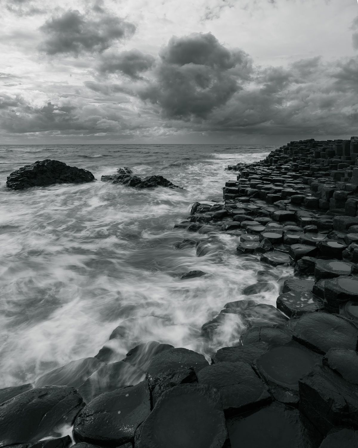 Dramatic black and white seascape of waves crashing over the hexagonal rocks at Giant's Causeway.