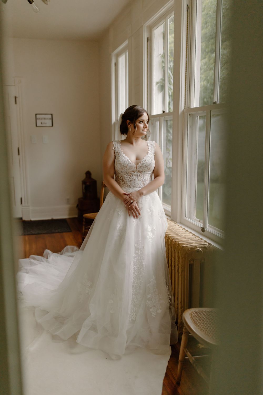 Full-length bridal portrait in a sunlit room showing flowing white wedding gown with train.