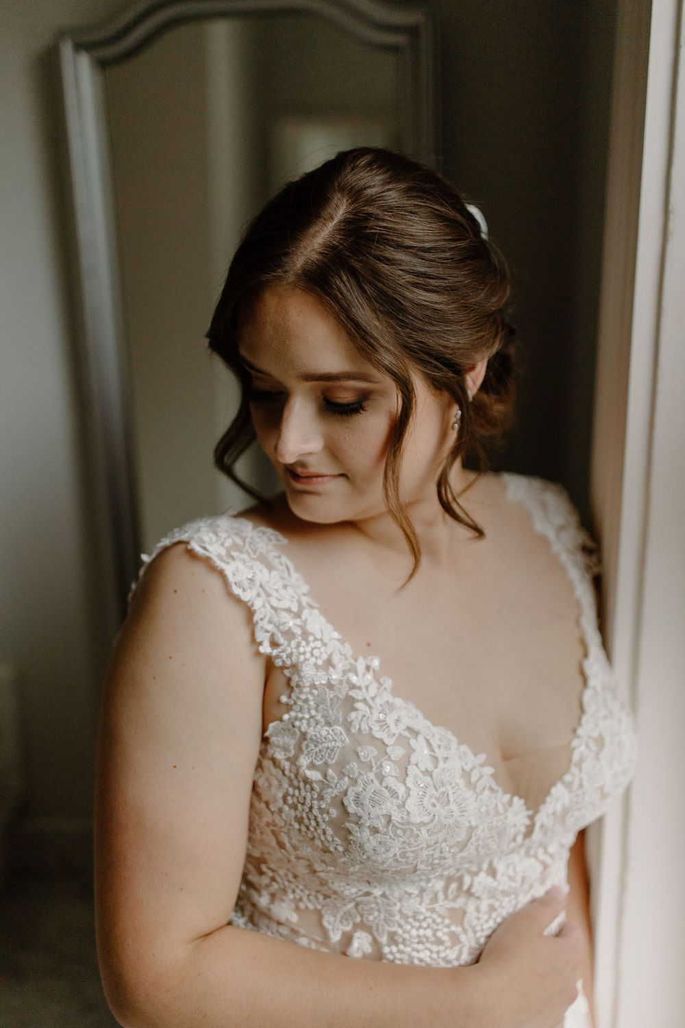 Bride in lace wedding dress looking down in soft window light.