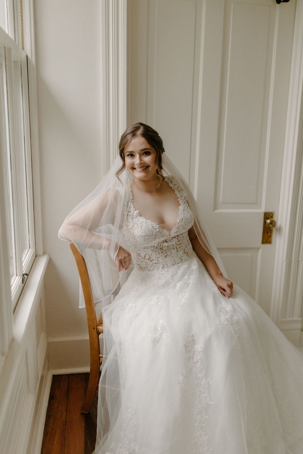 Joyful bridal portrait featuring detailed wedding gown with sweetheart neckline by sunny window.