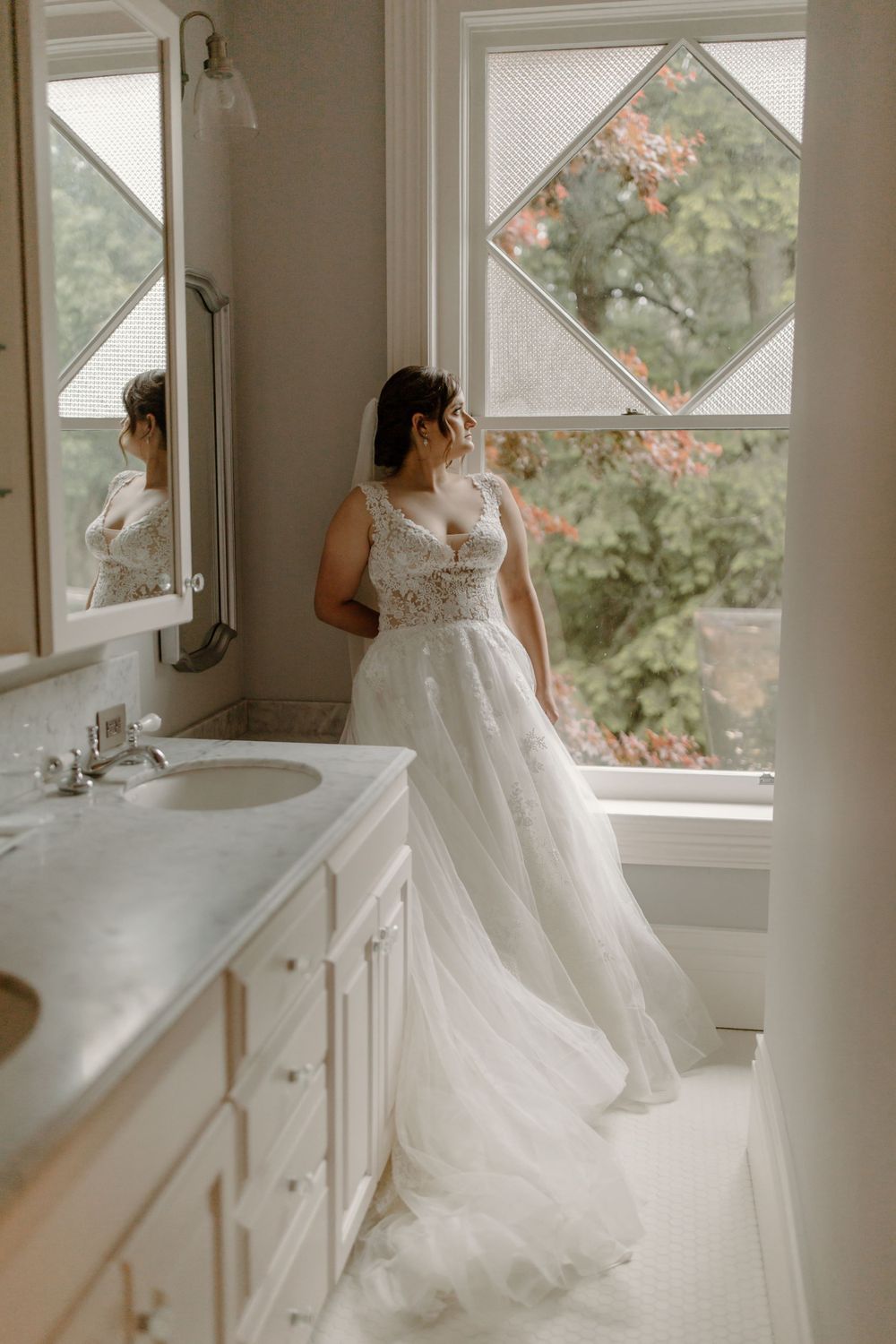 An elegant wedding dress with detailed lace bodice and flowing tulle skirt photographed in a bright bathroom.