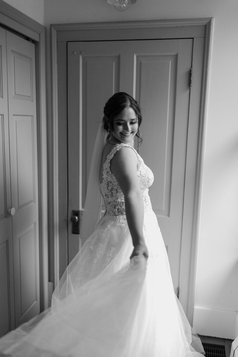 Beautiful wedding dress with lace details and flowing train photographed in black and white against a door.