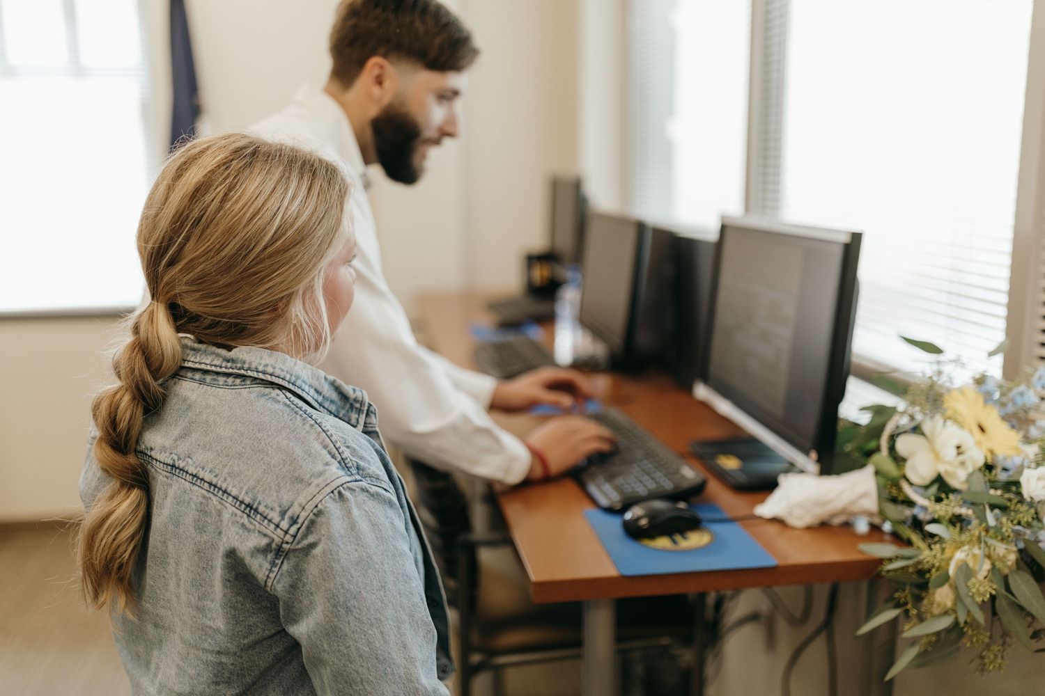 People collaborating at a desk with multiple computer monitors in a bright office setting.