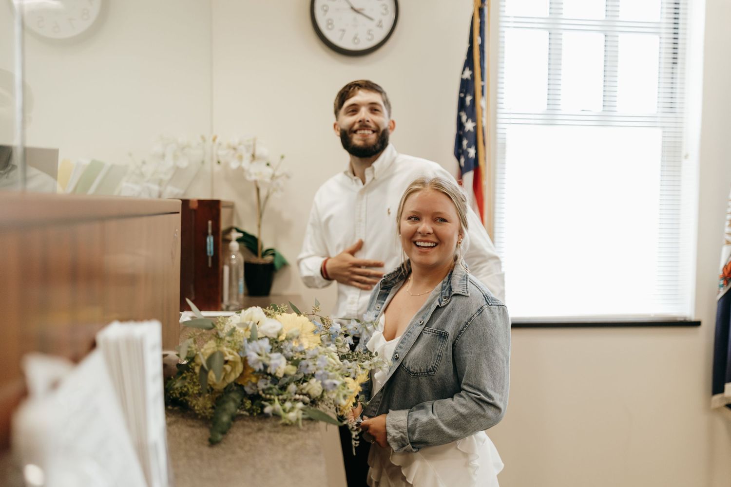 A joyful moment captured in an office setting with a US flag and floral arrangements.