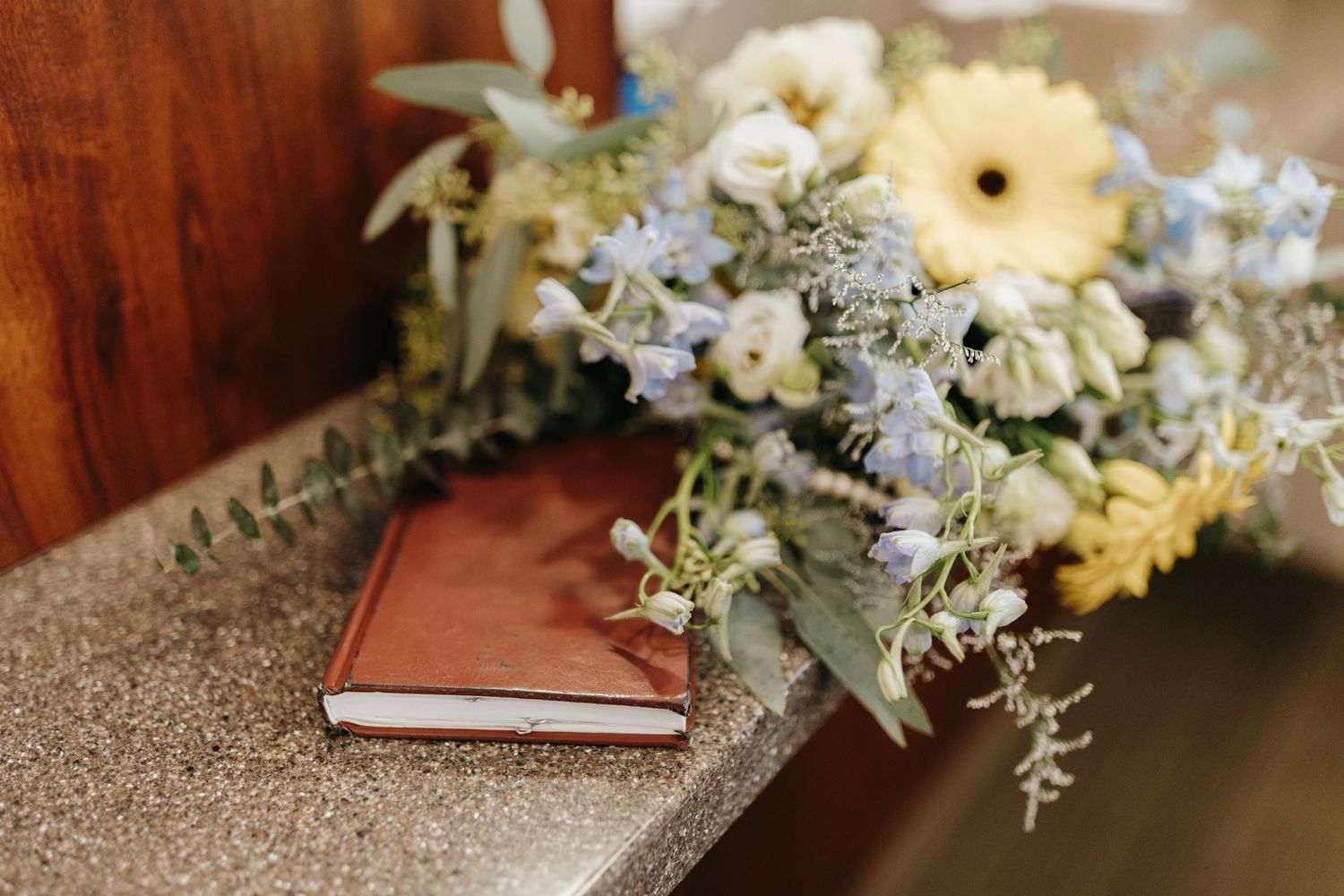 A delicate floral arrangement with white flowers and greenery rests on a leather-bound book.
