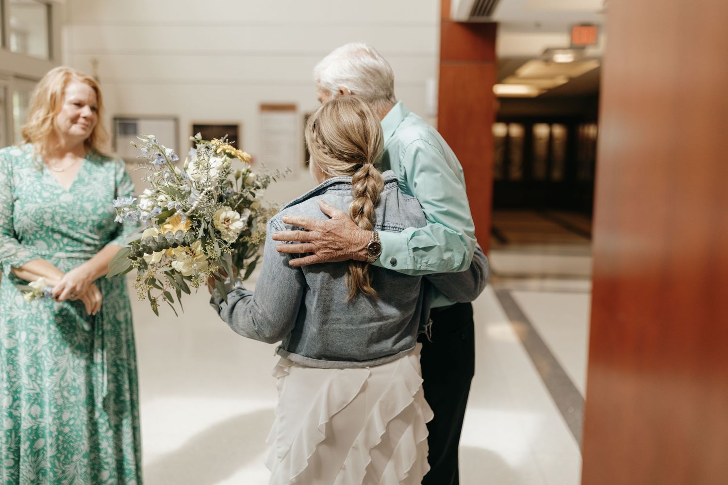A joyful group moment captured in a hallway with floral arrangements and formal dress attire.