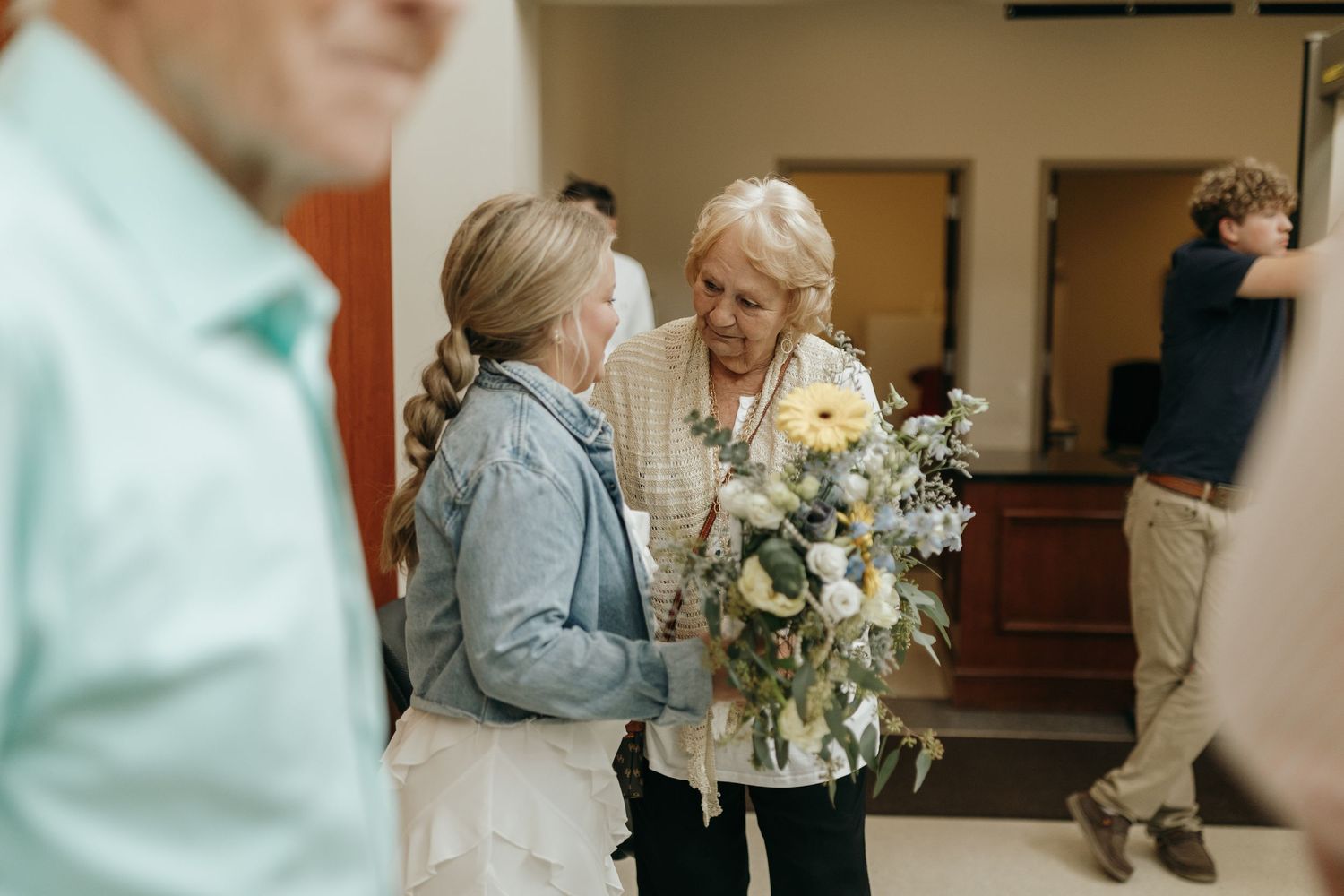 Two people chat while holding beautiful floral arrangements in an indoor hallway setting.