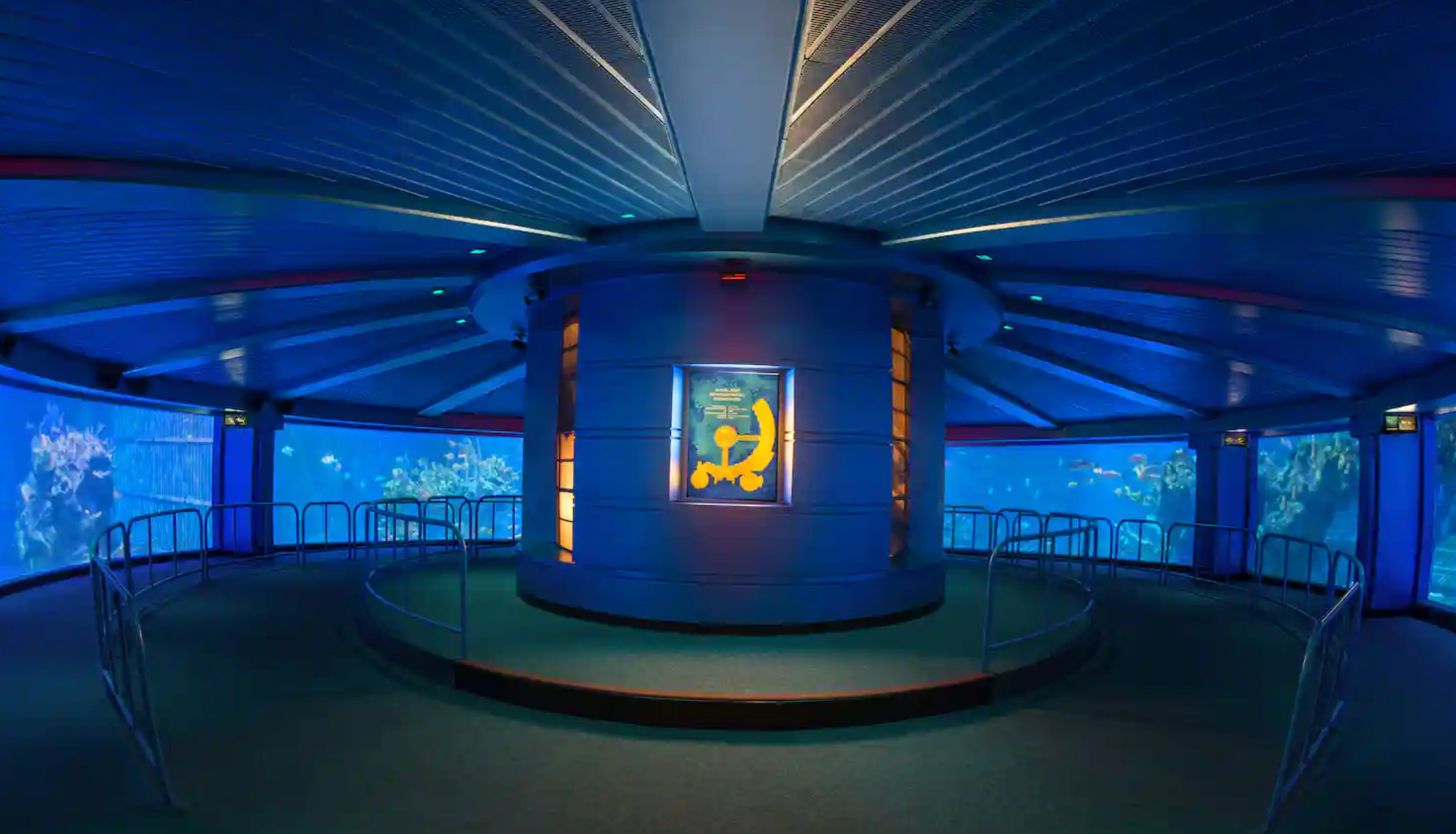 Panoramic view of a dimly lit blue circular exhibit room with glowing displays and screens on the walls.