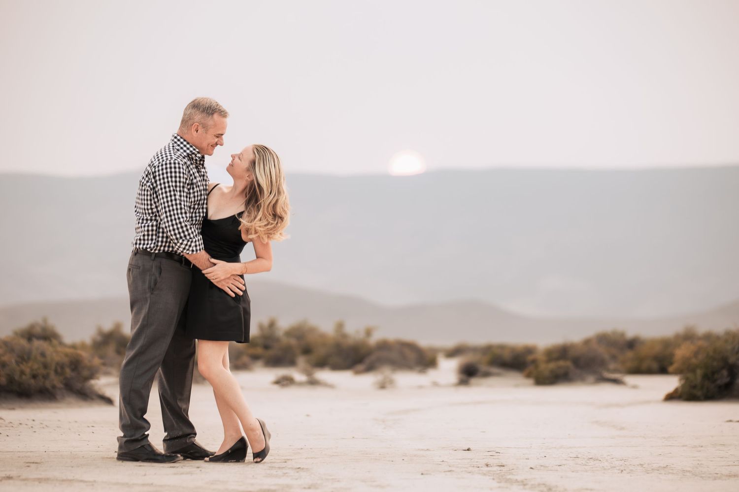 A couple embraces during a sunset photoshoot with mountain views in the background.