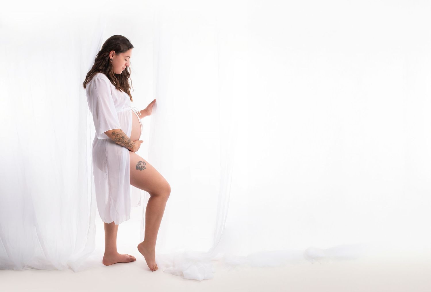 Ethereal maternity portrait with flowing white fabric against light background.