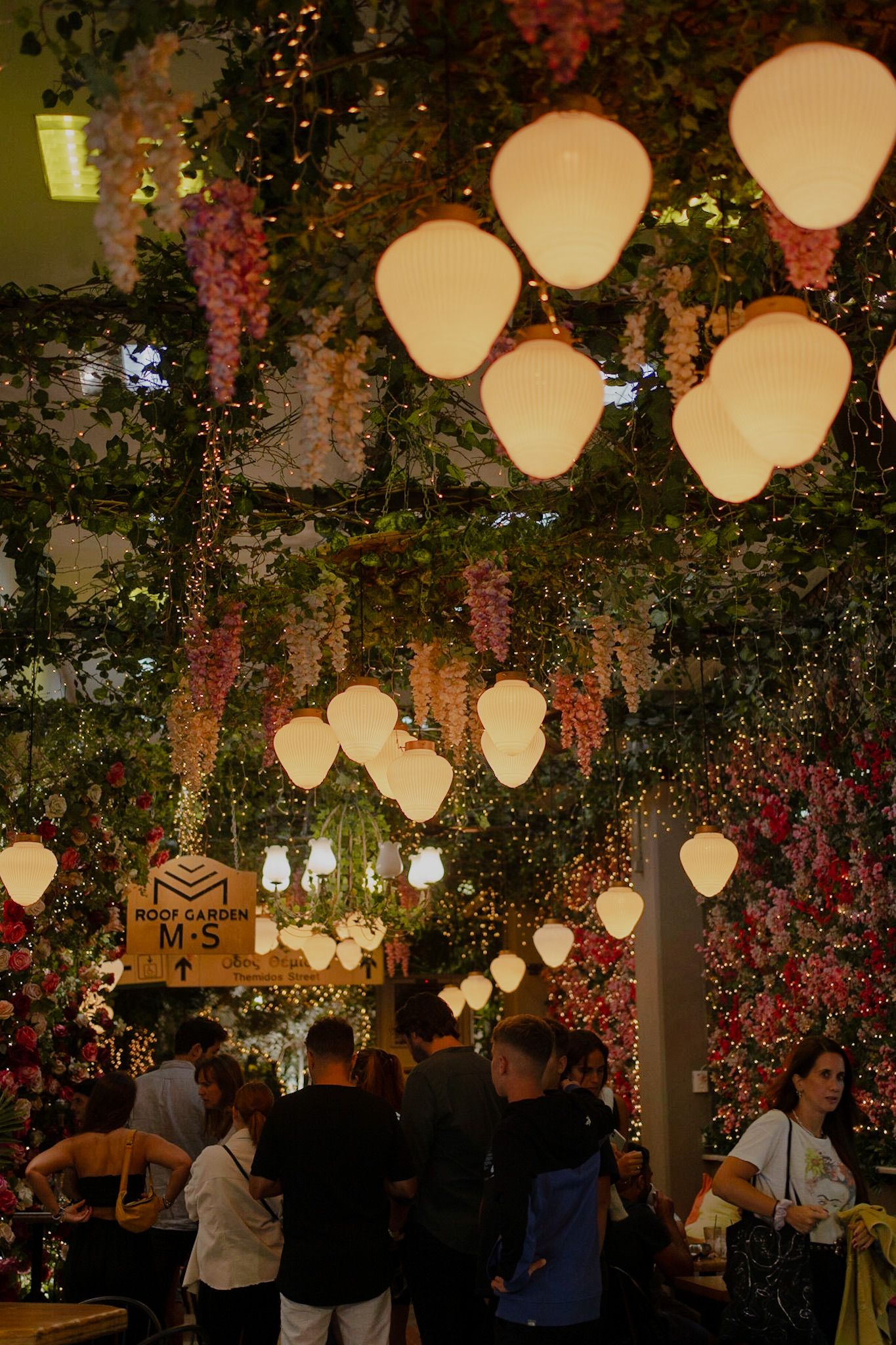 Indoor restaurant decorated with glowing lanterns, floral arrangements and hanging greenery creating a magical ambiance.