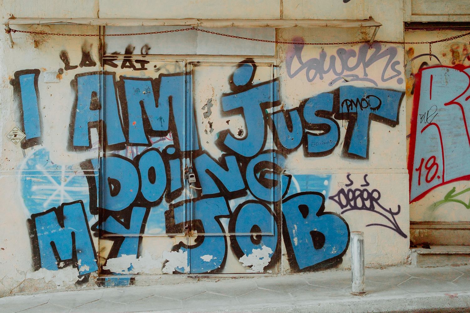 Blue graffiti text on a weathered wall reads 'I am just doing my job' in stylized urban street art lettering.