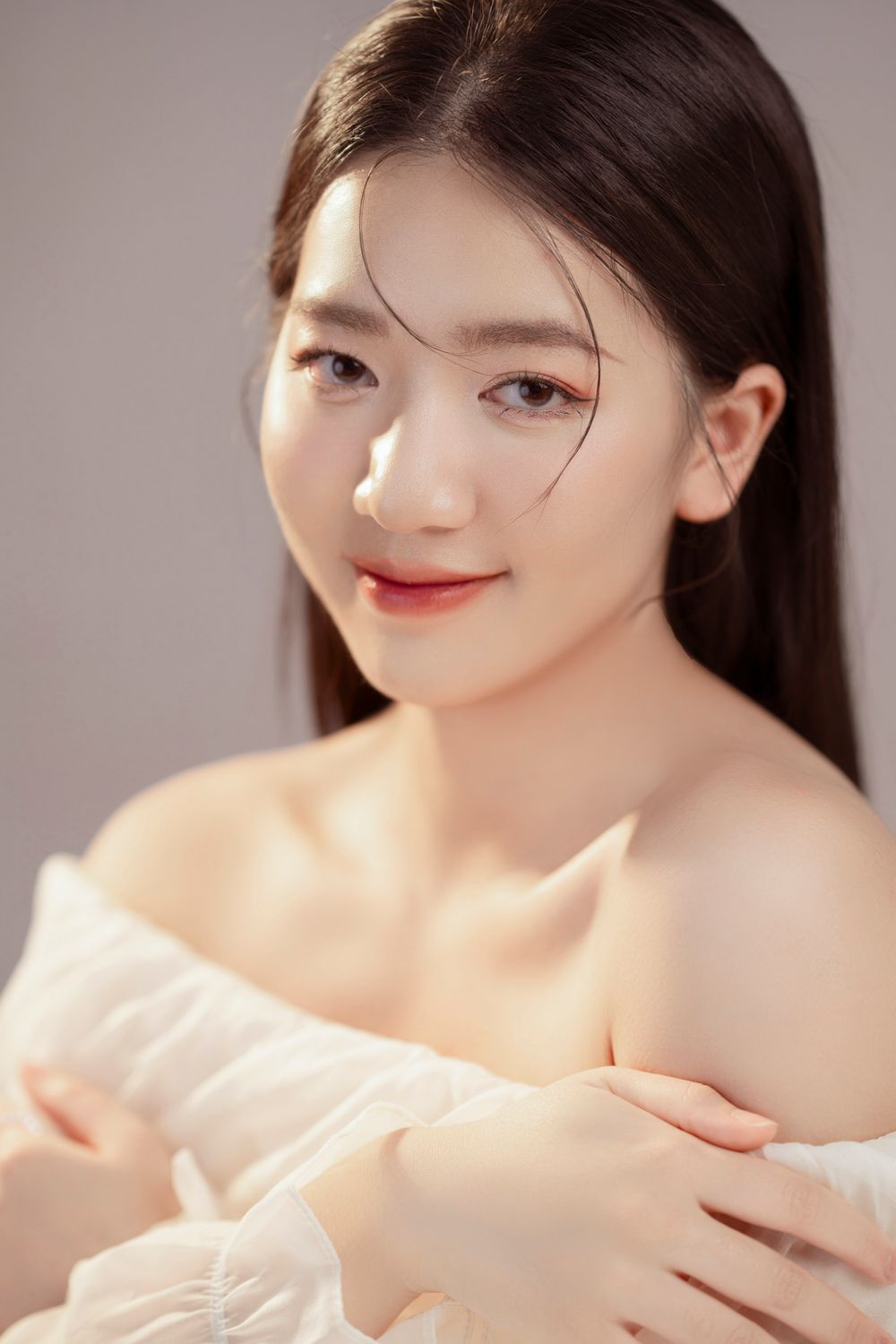Studio portrait featuring soft lighting and an elegant white off-shoulder top with natural makeup styling.
