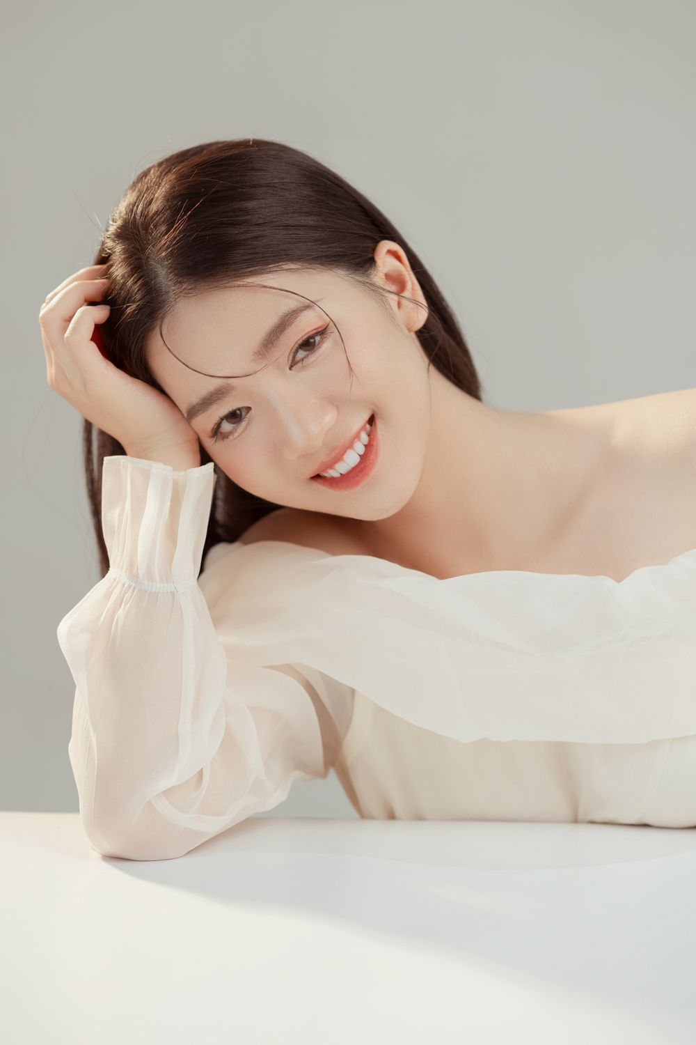 Beauty portrait with hand in hair showing natural makeup and white off-shoulder top.