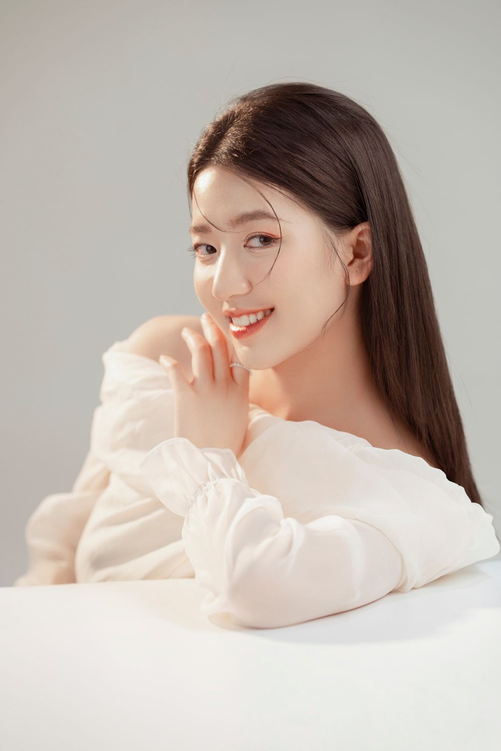 Portrait in soft white outfit against neutral background with gentle expression.