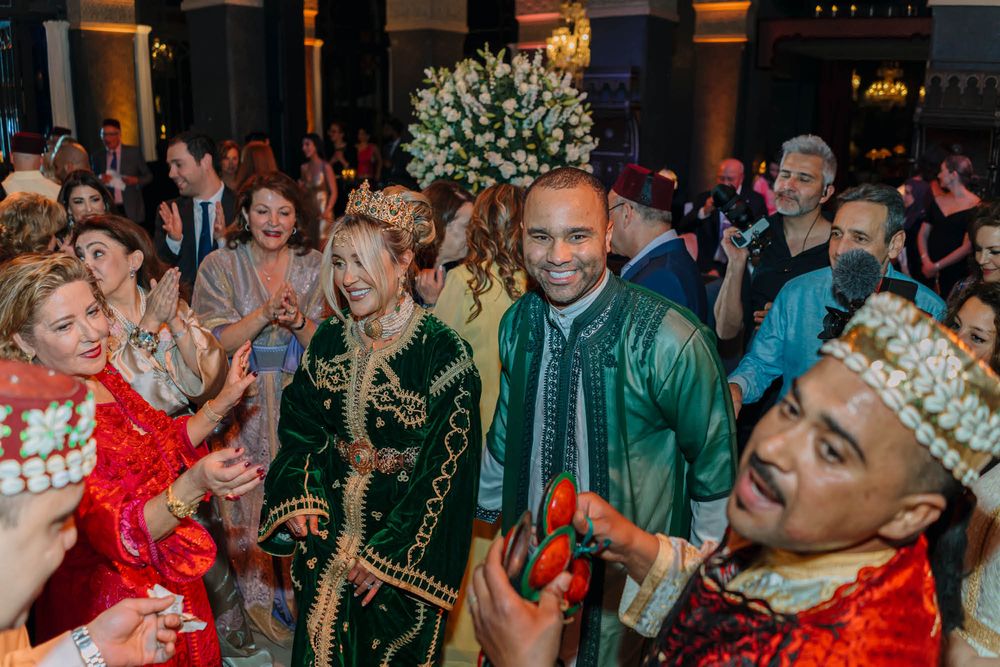 A lively wedding celebration with people in traditional Moroccan dress dancing and celebrating at an elegant venue.
