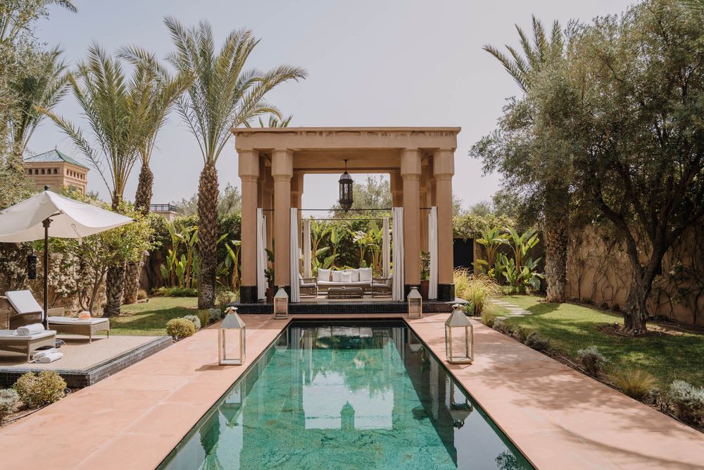 Luxurious swimming pool with a covered cabana and palm trees at a Moroccan resort.
