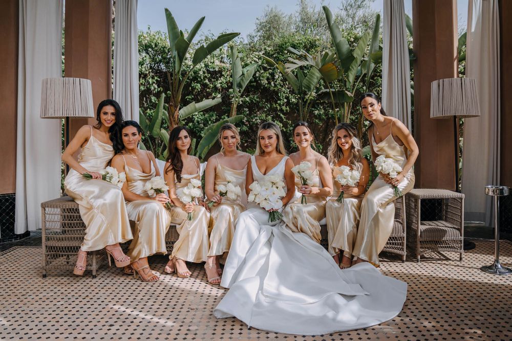 Group seated on chairs in a tropical setting wearing coordinated cream-colored outfits.