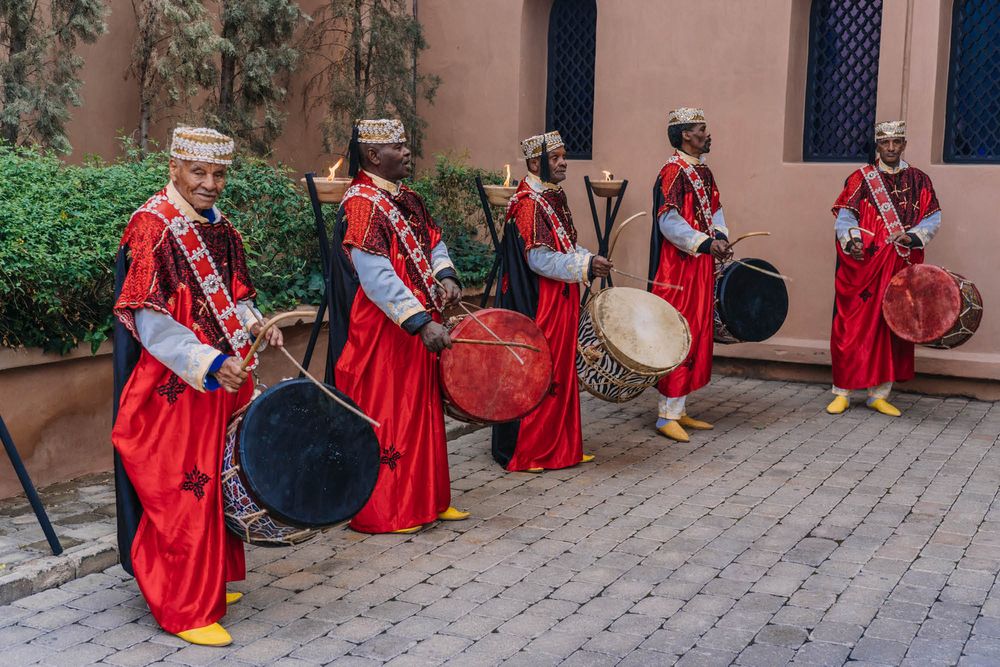 Traditional musicians in red ceremonial outfits perform with drums in line at a cultural festival.