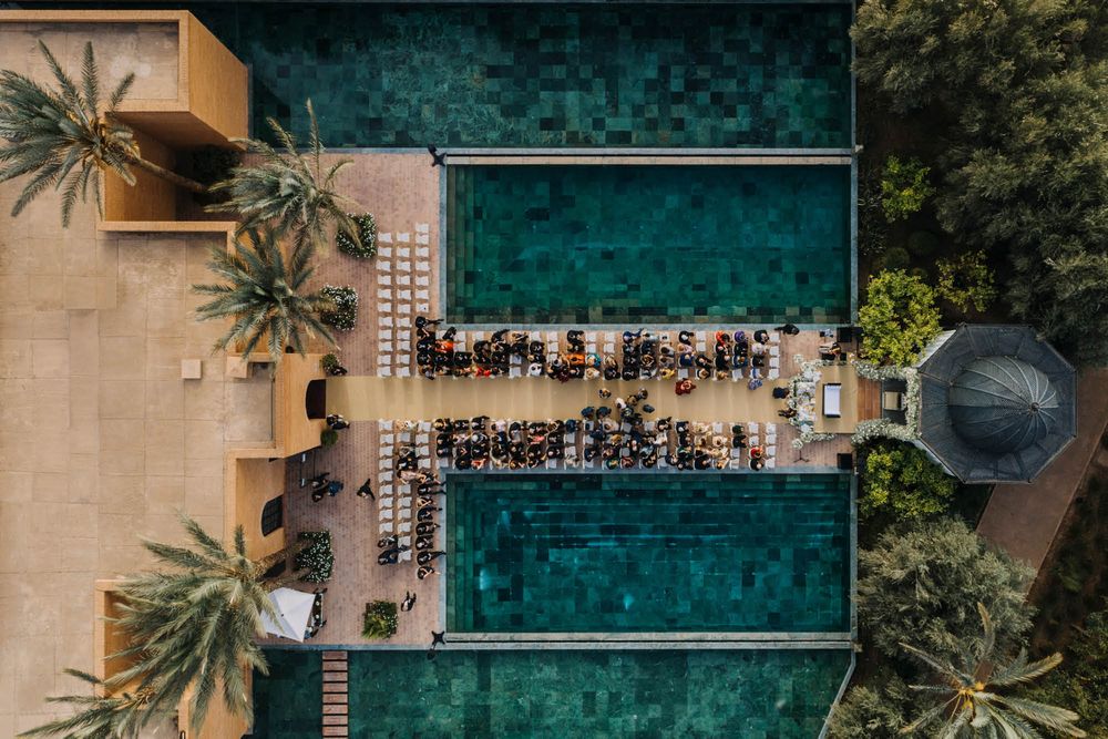 Aerial view of a turquoise swimming pool surrounded by lounge chairs and palm trees at a luxury resort.