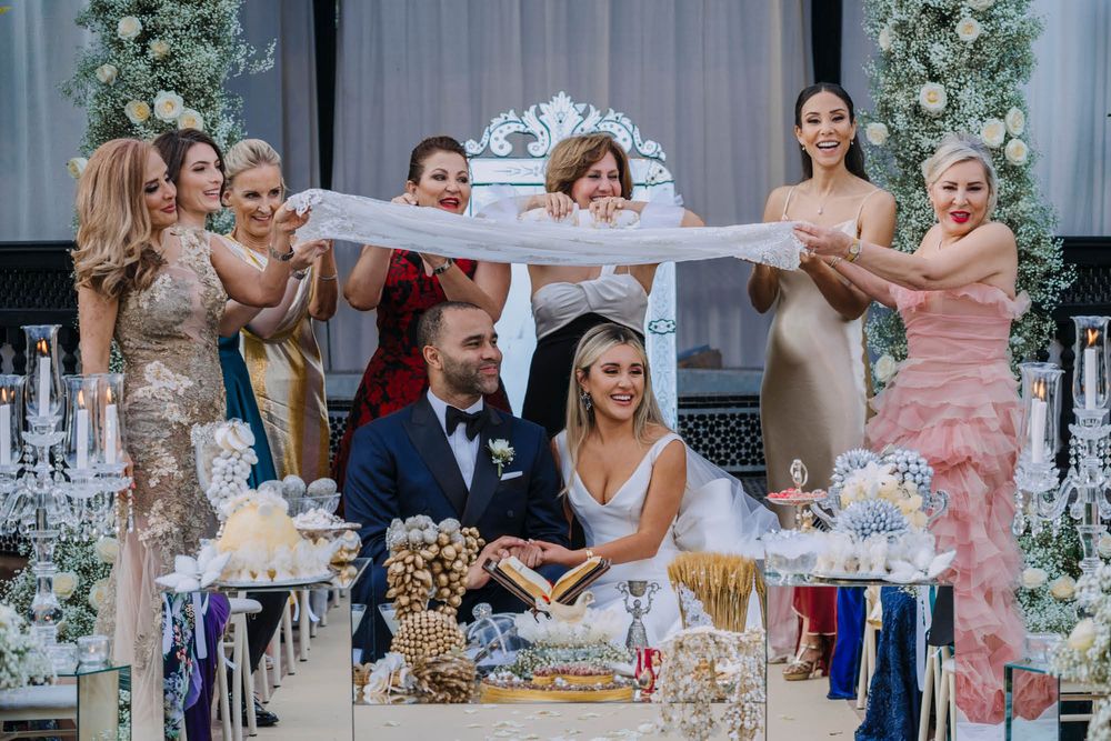 Wedding guests celebrate at an elegant reception with floral decorations while the couple cuts their cake.
