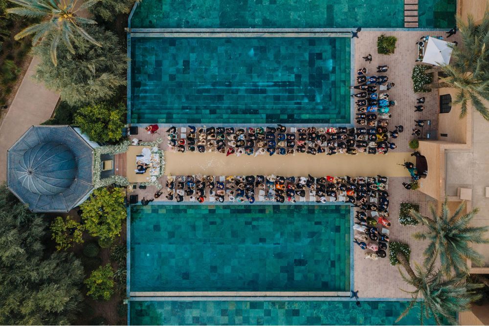 Aerial view of two turquoise swimming pools with beach chairs and tropical palm trees at a luxury resort.