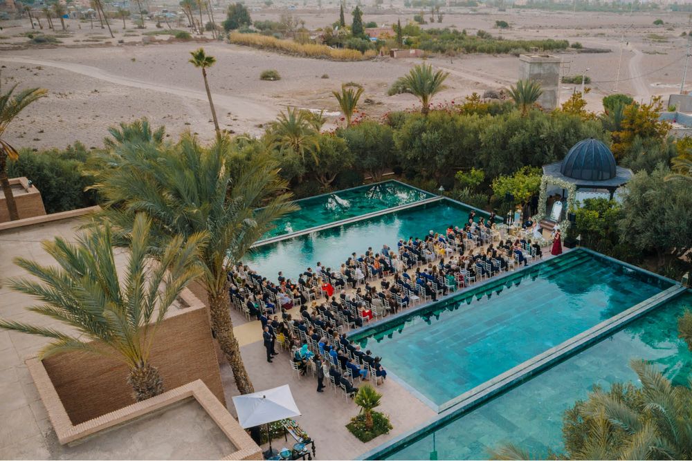 Aerial view of wedding ceremony seating arranged between two swimming pools at a luxury desert resort.