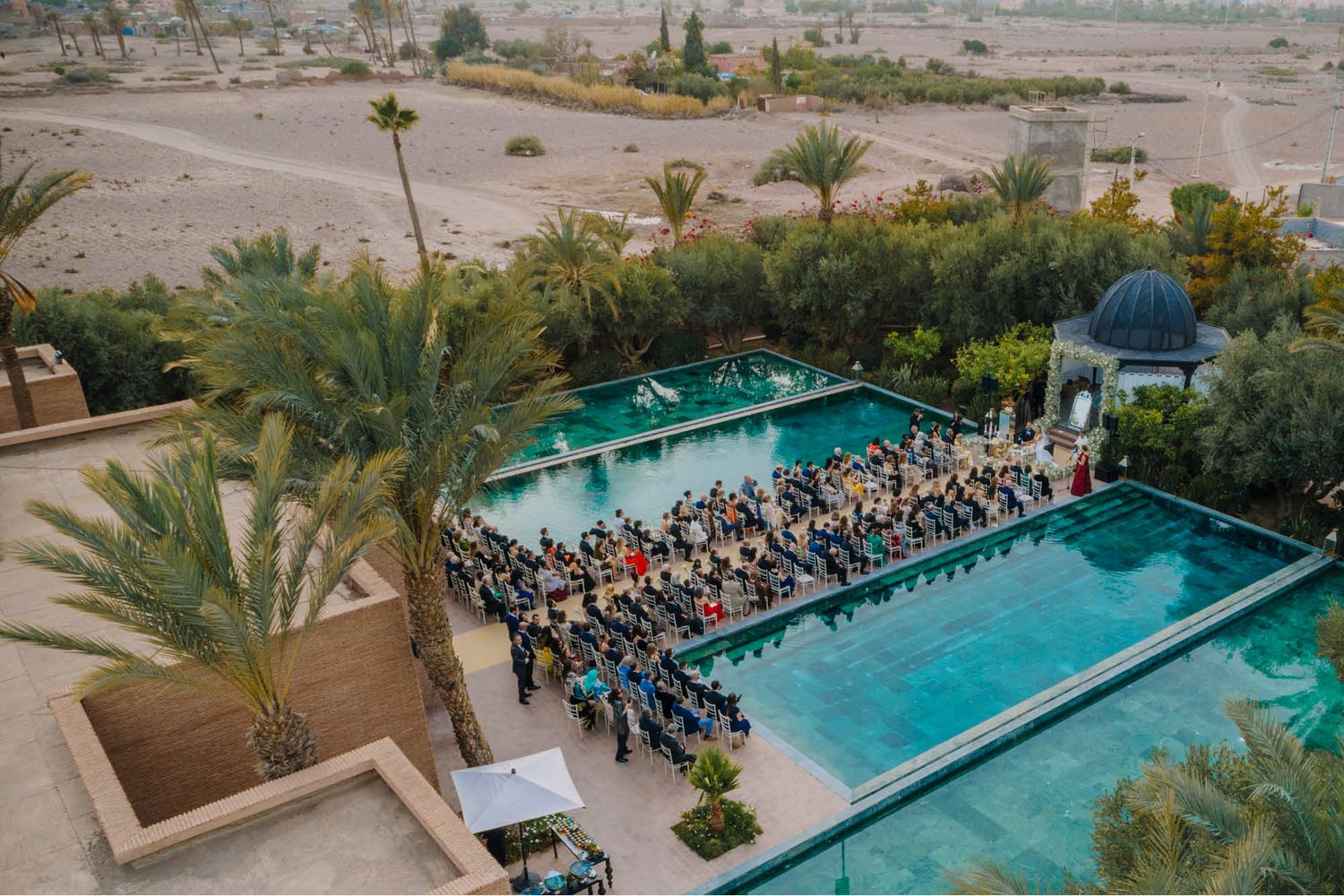 Aerial view of wedding ceremony seating arranged between two swimming pools at a luxury desert resort.