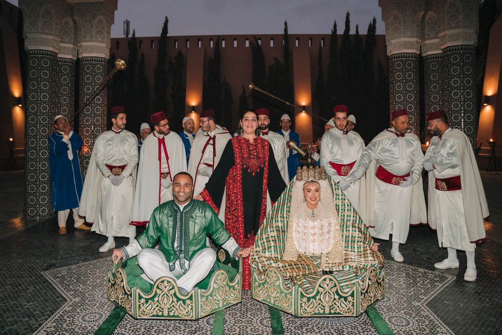 Traditional Moroccan performers in white and colorful robes gather for a ceremonial group photo.