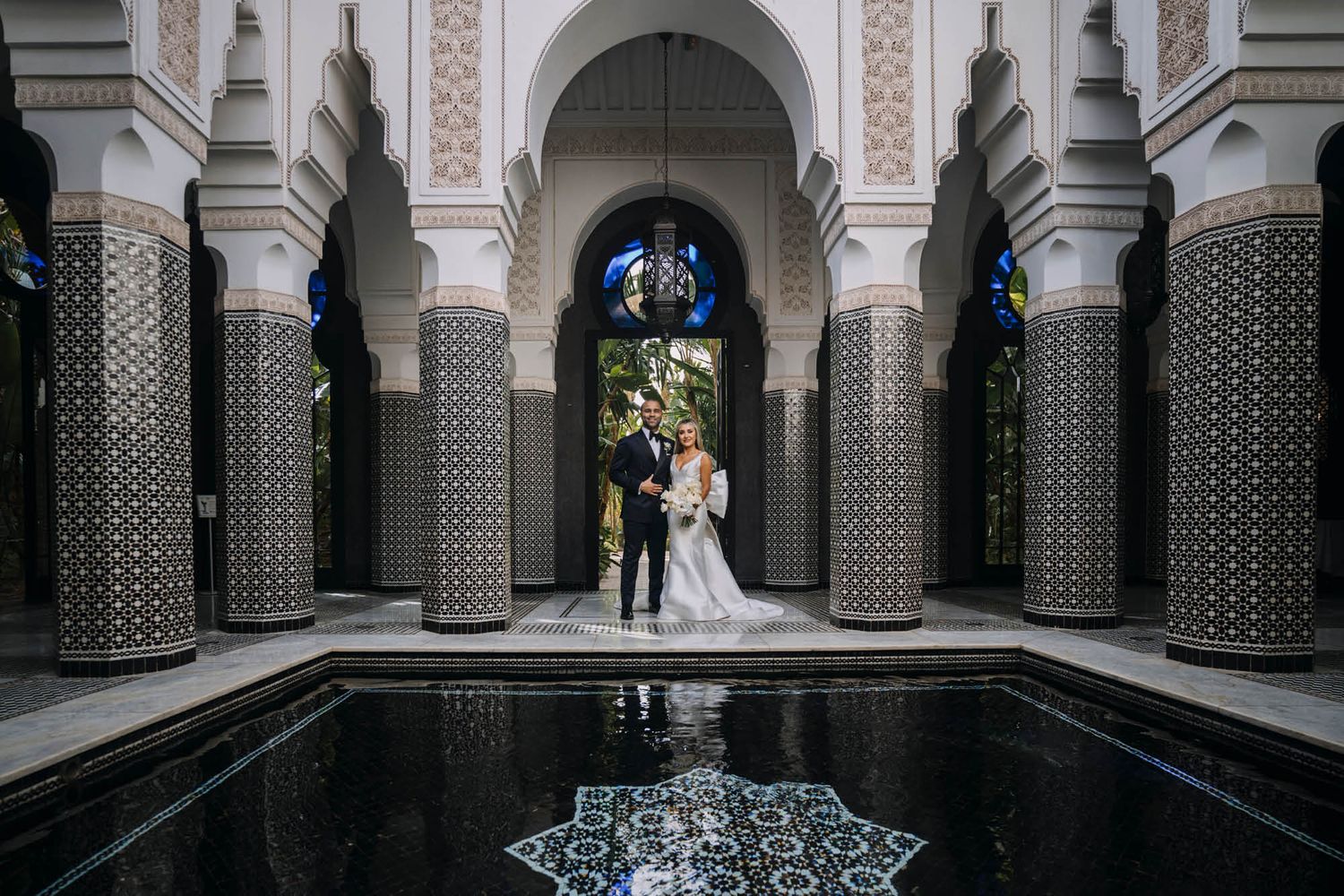 Elegant wedding ceremony setting at a Moroccan-style courtyard with ornate pillars and reflecting pool.