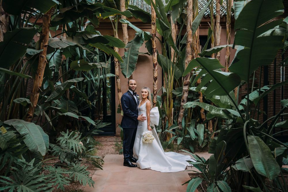 Wedding couple standing on pathway surrounded by lush tropical plants and banana trees.